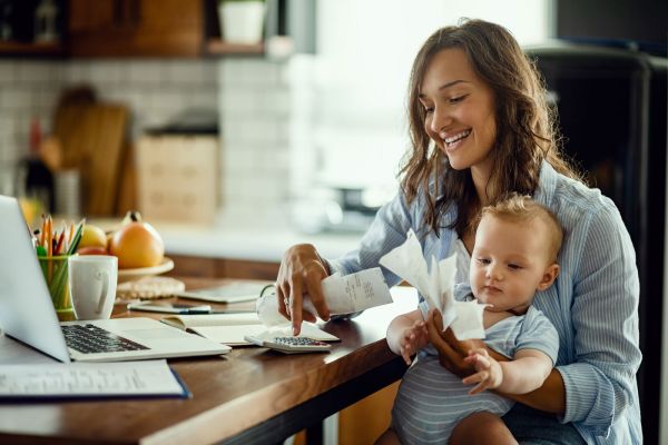 Young working mother with baby using calculator going through bills while calculating home finances